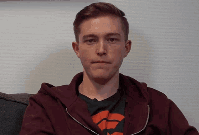 a young man wearing a maroon hoodie and a black shirt with an orange stripe on it
