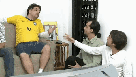 a man in a yellow shirt with the number 10 on it is sitting on a couch with two other men