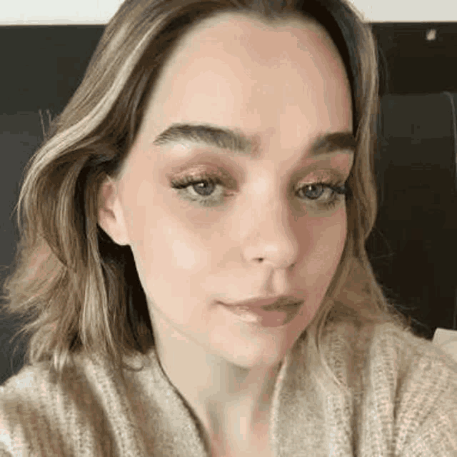 a close up of a woman 's face wearing a sweater and makeup .