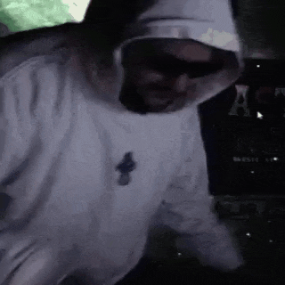 a man wearing sunglasses and a white hoodie is dancing in a dark room .
