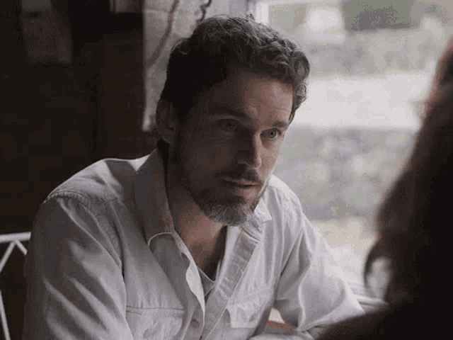 a man with a beard is sitting at a table with a woman and looking at her .