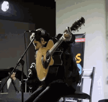 a man playing an acoustic guitar in front of a sign that says ' s ' on it