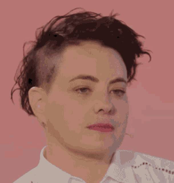 a close up of a woman 's face with a shaved head and a white shirt .
