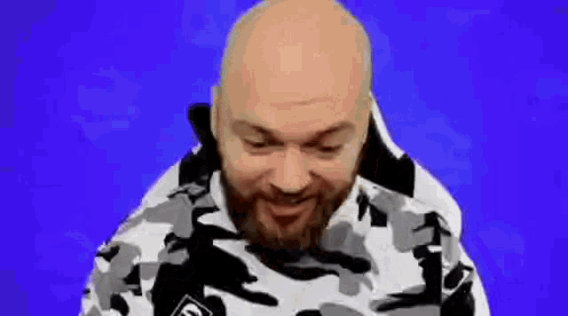 a bald man with a beard is wearing a camouflage hoodie .