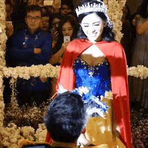 a woman wearing a tiara and a red cape is standing next to a man