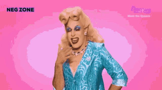 a drag queen in a blue shirt stands in front of a pink background that says neg zone on it