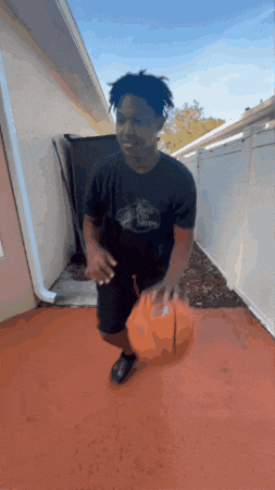 a man in a black shirt is dribbling a basketball on a red floor