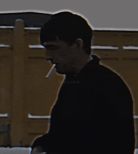a man is smoking a cigarette in front of a fence and the name branvik is on the bottom