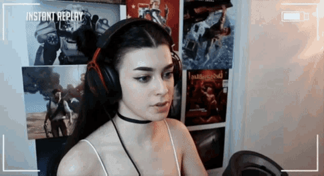 a woman wearing headphones and a choker is sitting in front of a screen that says instant replay