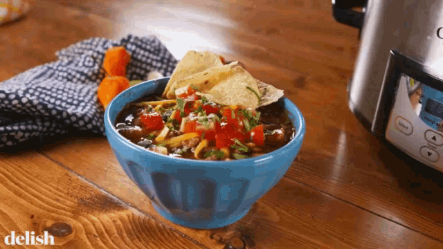 a bowl of soup with tortilla chips next to a crock pot that says delish