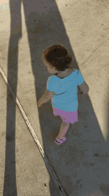 a little girl in a blue shirt and pink shorts walks on the sidewalk