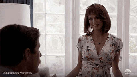 a man and a woman are standing next to each other in a living room . the woman is wearing a floral dress .