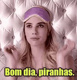 a woman wearing a purple sleep mask is laying on a bed and says bom dia piranhas .