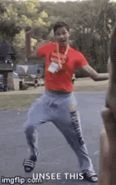 a man in a red shirt and gray sweatpants is dancing in a parking lot .