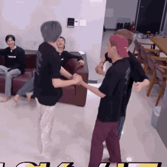 a group of people are dancing in a living room while a man in a pink hat sits on a couch .