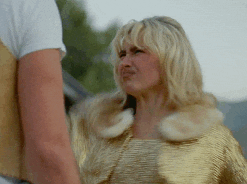 a blonde woman wearing a gold jacket is making a funny face