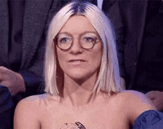 a naked woman wearing glasses and a ring is sitting in a crowd .