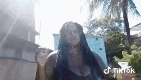 a woman with braids is standing in front of a palm tree with a tiktok logo in the corner .