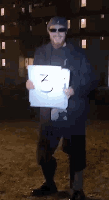 a man wearing sunglasses and a hat is holding a piece of paper with the number 3 written on it