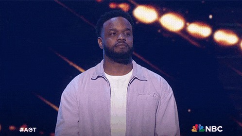 a man in a purple jacket stands on a stage with a nbc logo in the corner