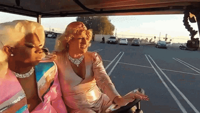 two drag queens are sitting in the back seat of a golf cart