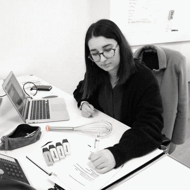 a woman sits at a desk with a laptop and a bunch of stabilo markers on it