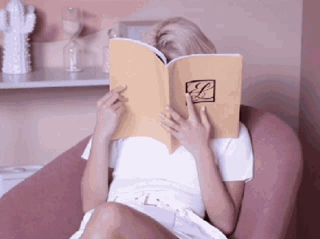 a woman sits in a chair reading a book with the letter l on it