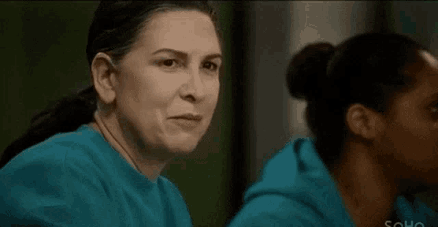 two women in blue scrubs are sitting next to each other .