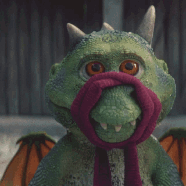 a green stuffed dragon with a purple scarf around its mouth
