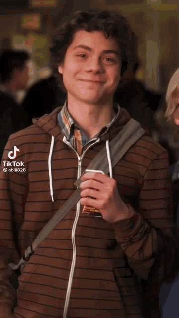 a young man in a striped shirt is smiling while holding a cup of coffee .