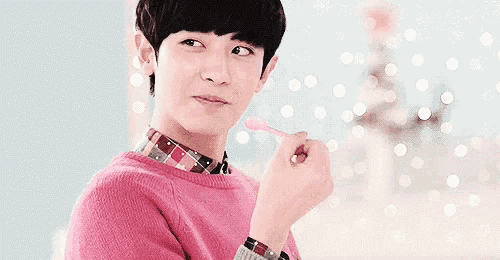 a young man in a pink sweater is eating a pink lollipop with a spoon .
