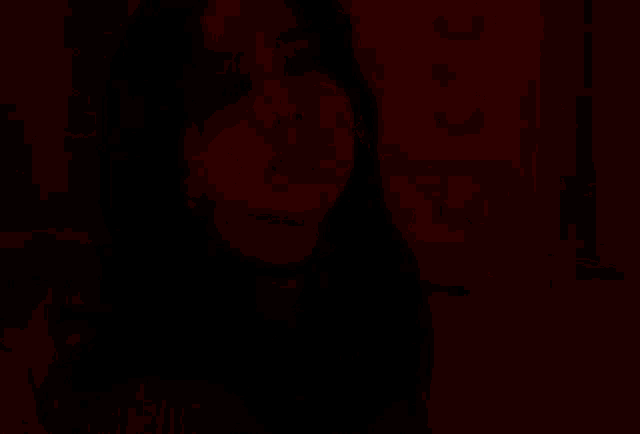 a woman in a red sweater looks at the camera in a dark room