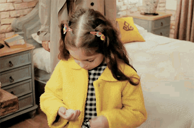 a little girl wearing a yellow coat has a clip in her hair with the letter b on it