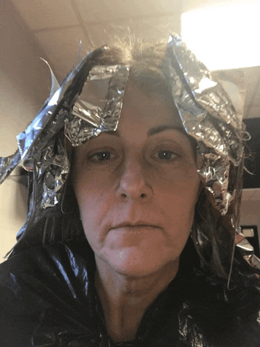 a woman with aluminum foil wrapped around her head looks at the camera