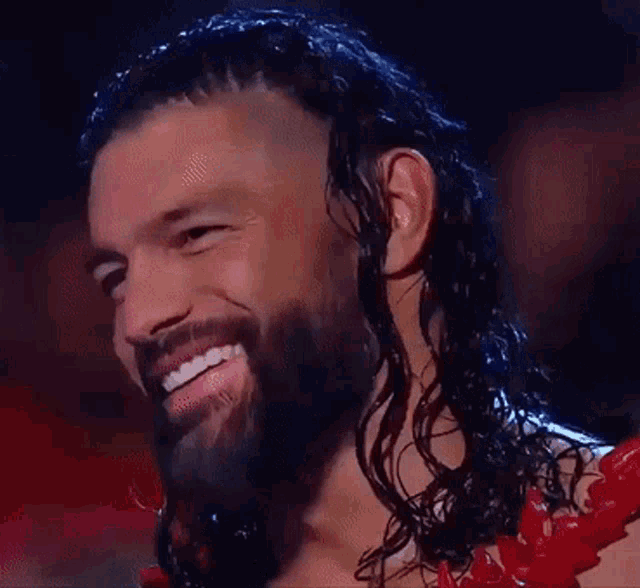 a man with long hair and a beard is smiling while wearing a red lei .