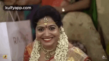 a bride is smiling for the camera while wearing a necklace and a garland around her neck .