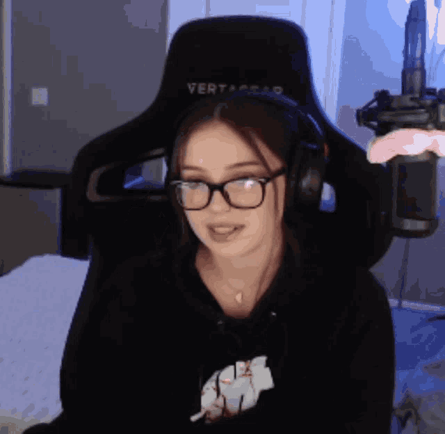a woman wearing glasses and headphones is sitting in a chair that says vertagear