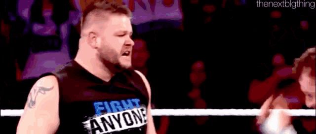 a wrestler wearing a shirt that says fight anyone is standing in a ring .