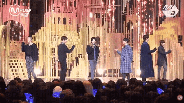 a group of men are standing on a stage in front of a crowd with a microphone in their hand