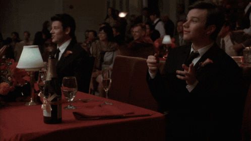 a man in a tuxedo sits at a table with wine glasses and a bottle of champagne