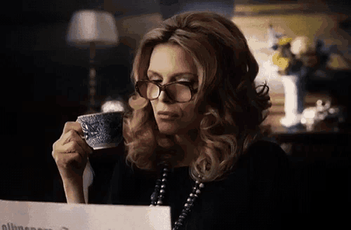 a woman wearing glasses is drinking a cup of coffee and reading a newspaper