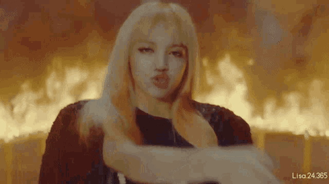 a woman with long blonde hair is standing in front of a fire .