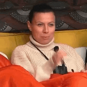 a woman in a turtleneck sweater is sitting on a couch holding a remote control .