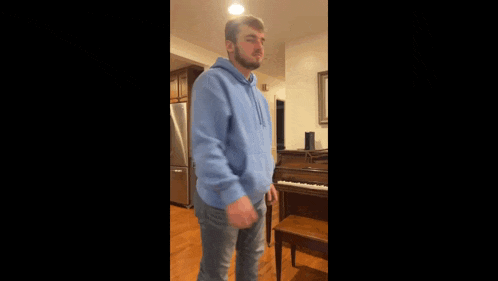 a man wearing a blue hoodie is standing in front of a piano .
