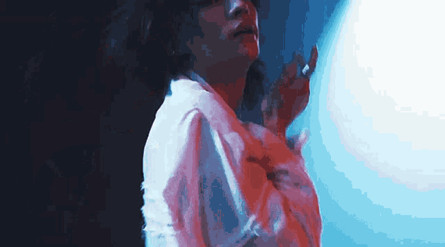 a woman in a white shirt is standing in front of a blue light and smoking a cigarette .