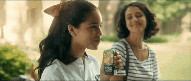 two girls are sitting next to each other and one of them is holding a box of crystal light juice .