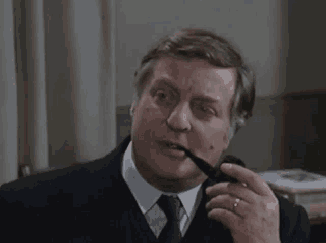 a man in a suit smoking a pipe with a ring on his finger