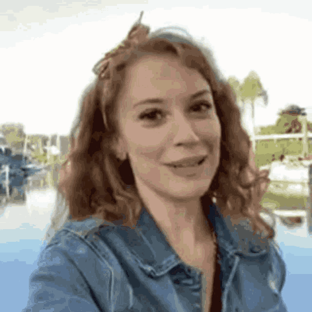 a woman in a denim jacket is taking a selfie with a boat in the background .