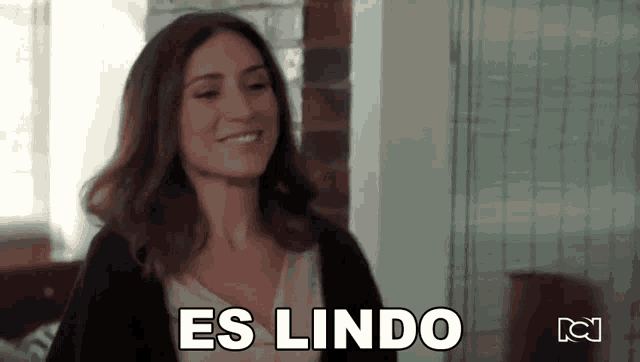 a woman is smiling and saying `` es lindo '' while standing in a room .