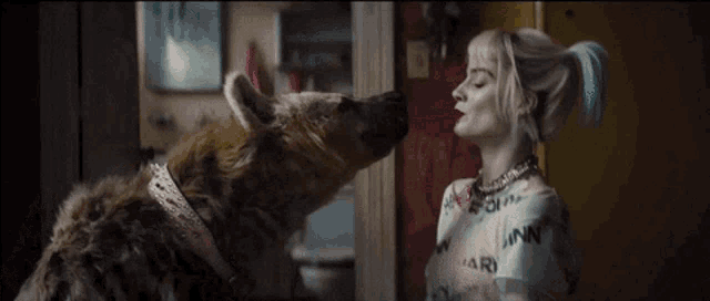 a woman with harley quinn written on her shirt is being kissed by a hyena